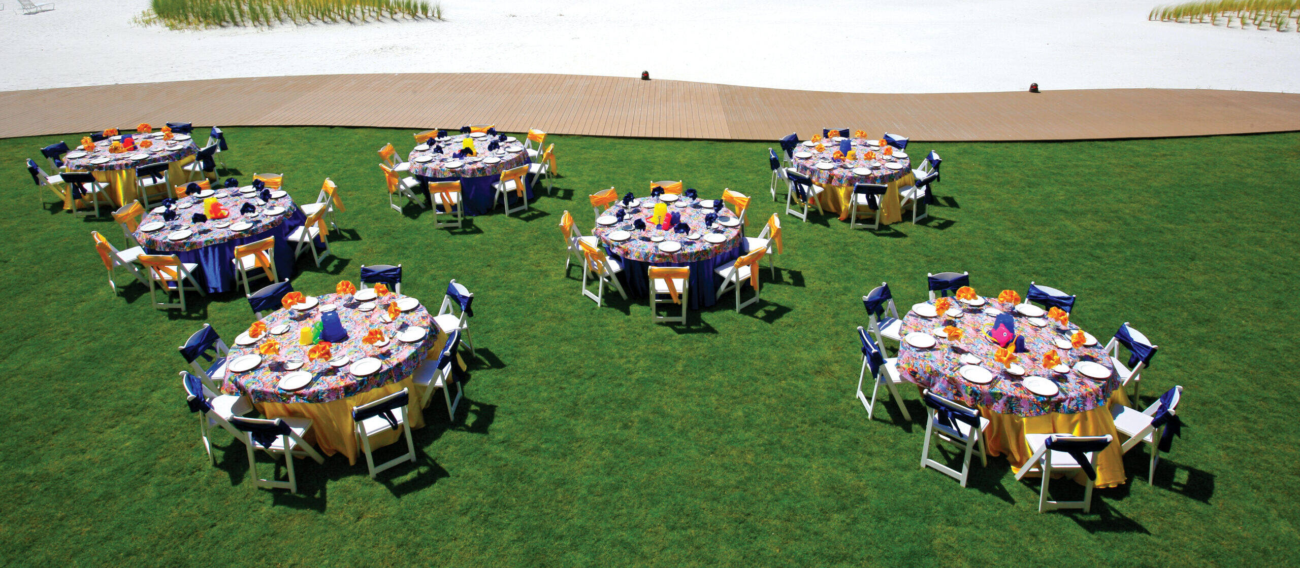 Eight round tables with colorful tablecloths and place settings are arranged on a grassy lawn at Sandpearl Resort in Clearwater Beach, Florida.