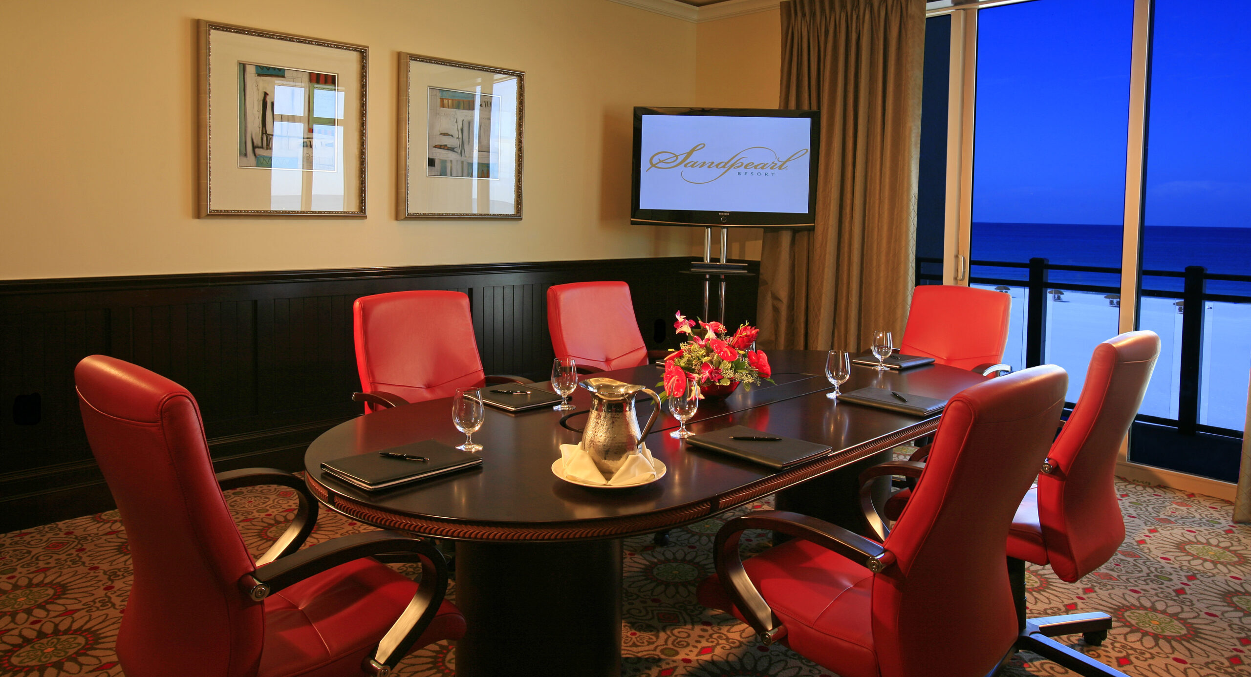 A conference room with a dark oval table surrounded by six red chairs at Sandpearl Resort in Clearwater Beach, Florida.