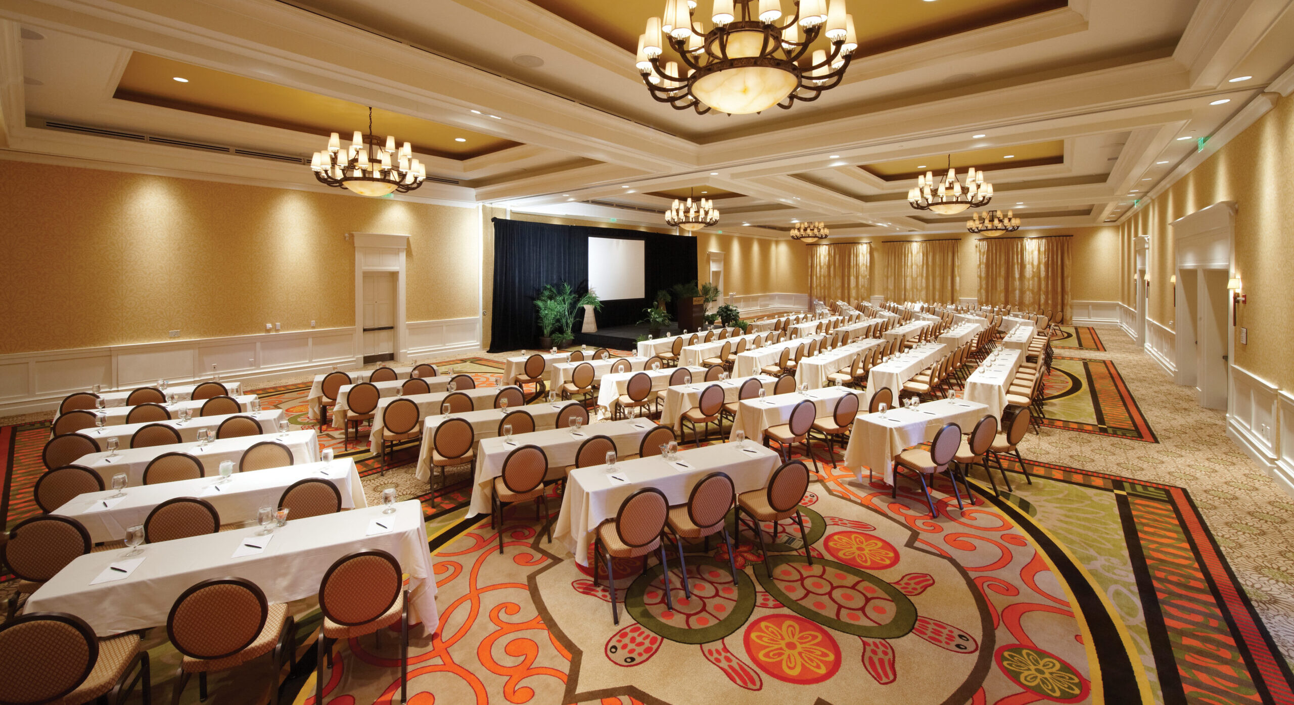 A spacious conference room features rows of white-covered tables and tan chairs facing a presentation screen at Sandpearl Resort in Clearwater Beach, Florida.