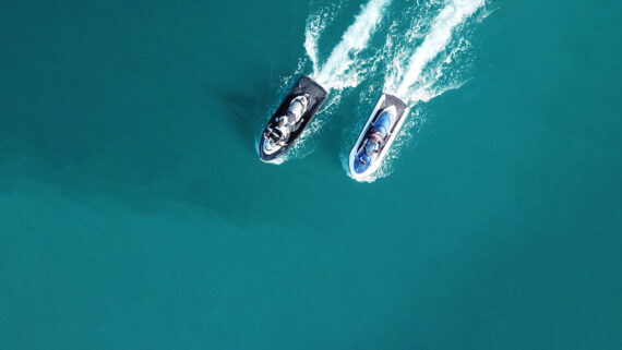 Aerial view of two people riding jet skis side by side, leaving white trails on bright blue water.