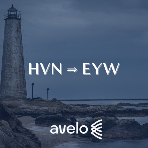 A tall lighthouse stands on a rocky shore under a cloudy sky. Text in the center reads HVN ⇒ EYW and the Avelo Airlines logo is at the bottom.