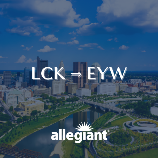 Downtown cityscape with skyline, river, and green spaces. Overlaid text reads “LCK ⇒ EYW” and “allegiant®,” indicating a flight route, with a bright blue sky and scattered clouds above.