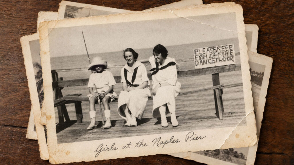 Three girls in vintage clothing sit on a wooden pier by the sea. A sign behind them reads Please keep feet off the dance floor. The photo is labeled Girls at the Naples Pier..