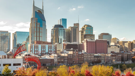 Downtown Nashville skyline with modern and historic buildings, including the AT&T Building, under a clear blue sky and autumn trees in the foreground.