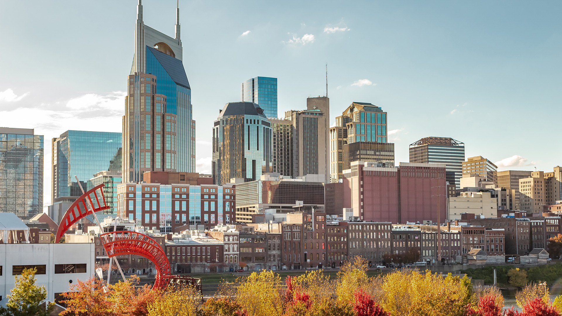 Downtown Nashville skyline with modern and historic buildings, including the AT&T Building, under a clear blue sky and autumn trees in the foreground.