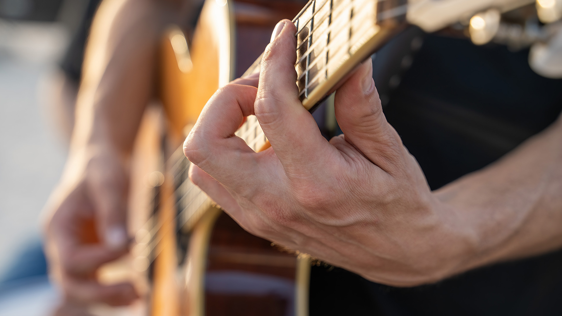 Close-up of a persons hand pressing fingers onto the fretboard of an acoustic guitar.