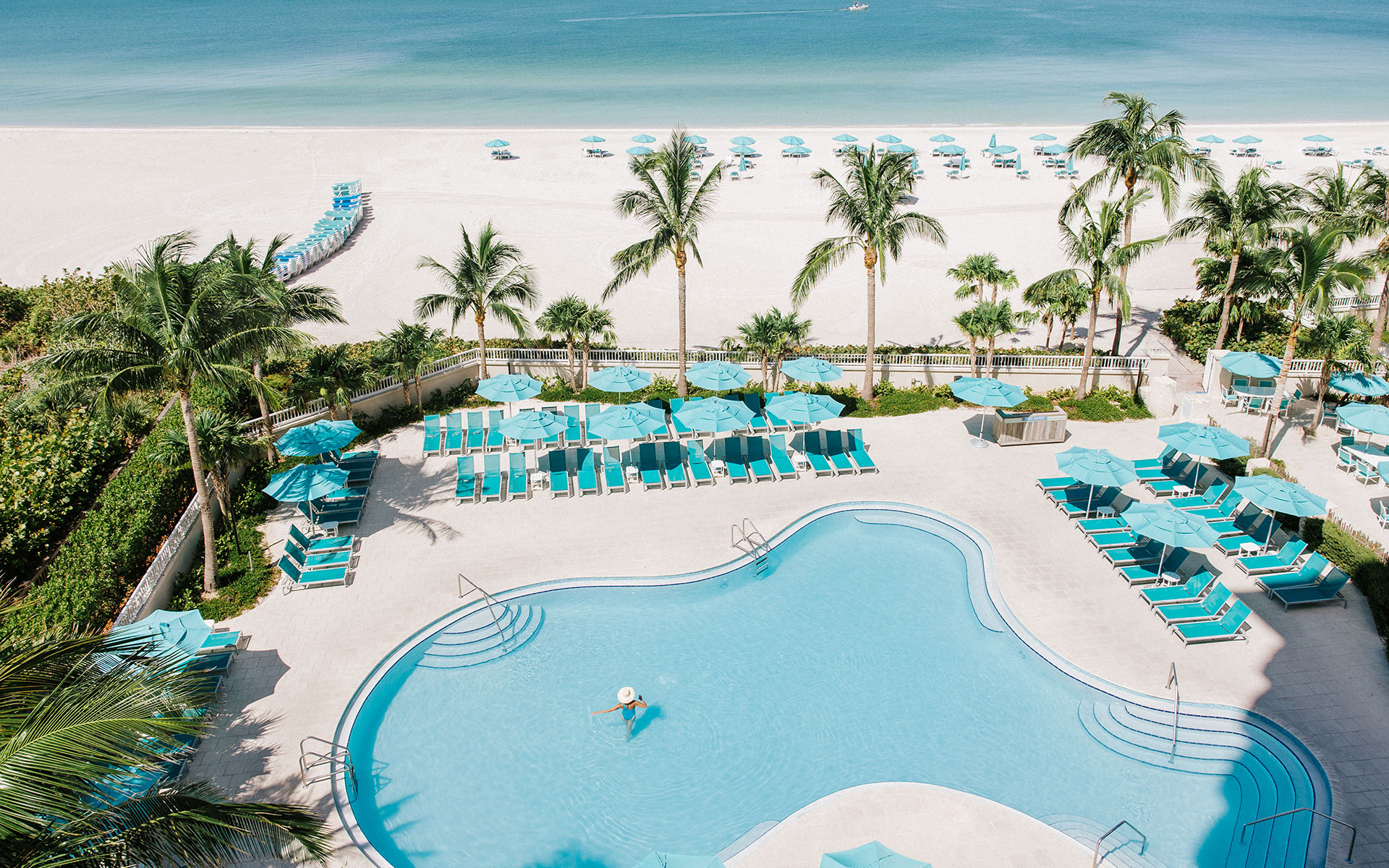 Aerial view of a beachfront hotel pool with a single person in the water at Lido Beach Resort.