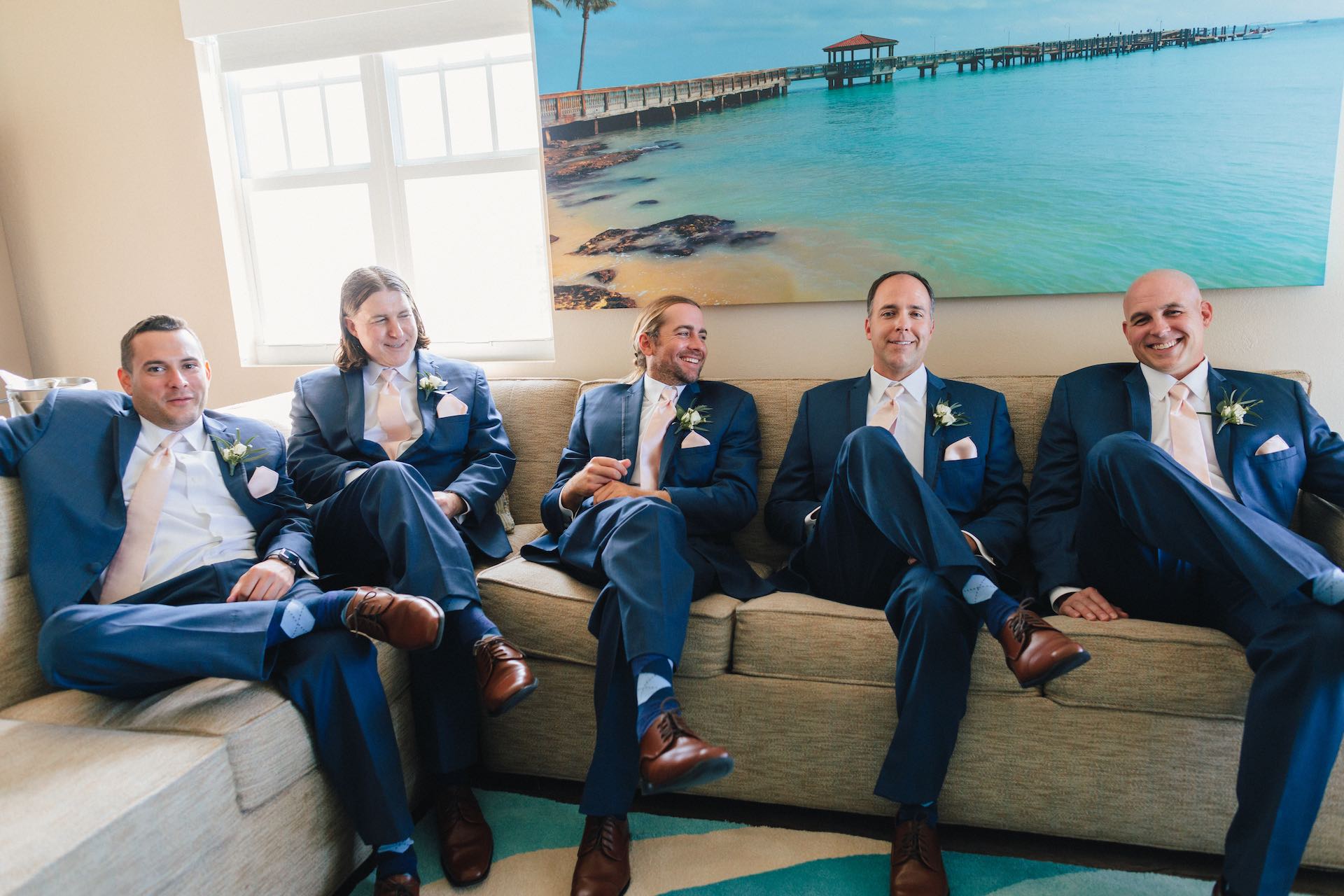 Five men in suits sitting on a couch in a lounge area.