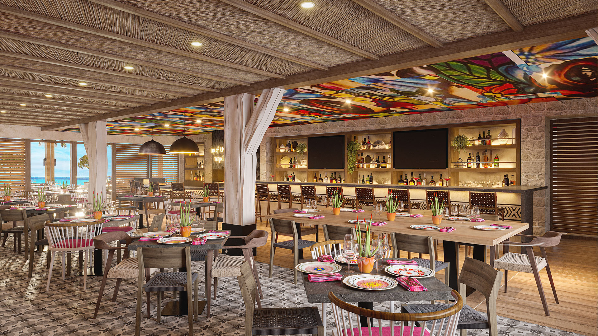 A vibrant restaurant interior with colorful plates on wooden tables, patterned chairs, a decorative bar area, patterned tile floors, and a ceiling with colorful floral art. Large windows reveal a beach and ocean view outside.