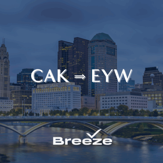 Breeze Airways advertisement showing CAK to EYW flight route over a city skyline with tall buildings and a bridge at dusk.