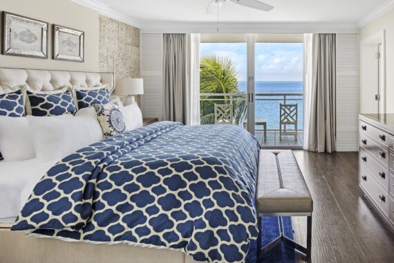 Hotel room featuring a king bed with a blue and white patterned duvet, overlooking a balcony with an ocean view.