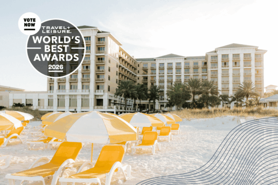 A beachfront hotel with yellow and white lounge chairs on sandy shore, palm trees, and a Travel + Leisure World’s Best Awards 2026 badge in the corner.