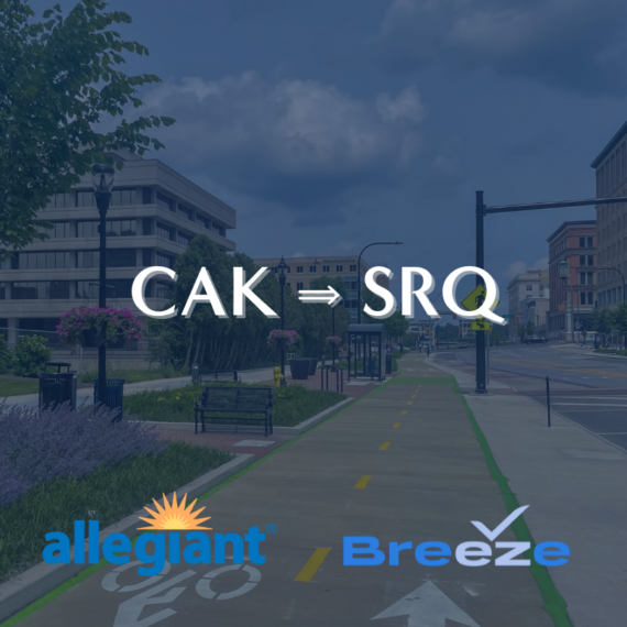View of an urban street with bike lanes and greenery. Text in the sky reads CAK ⇒ SRQ. Logos for Allegiant and Breeze are on the road, representing airlines. The scene is bright under a cloudy sky.