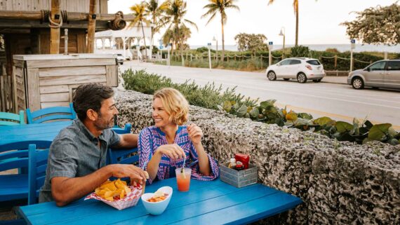 A couple enjoying food and drinks, smiling at Sandbar restaurant in Delray Beach.