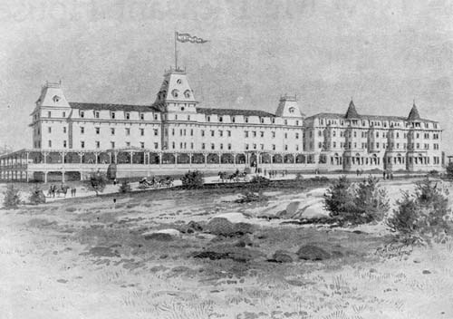 A historic black and white illustration of a large, grand hotel with multiple stories and distinctive towers. The building features a long veranda and a central flag atop the roof. There are carriages and people in the foreground.