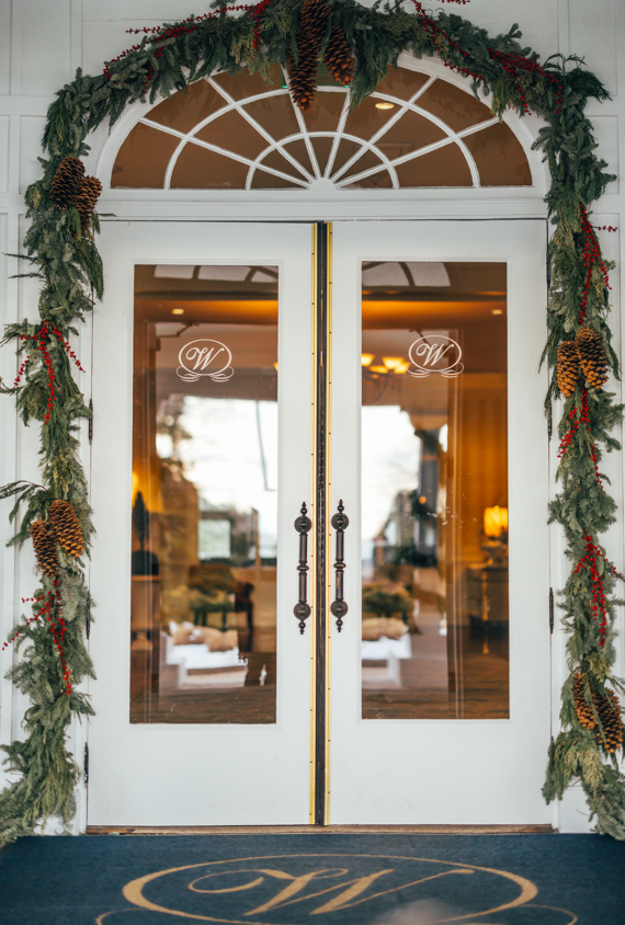Double glass entry doors decorated with a festive evergreen garland featuring pinecones and red berries.