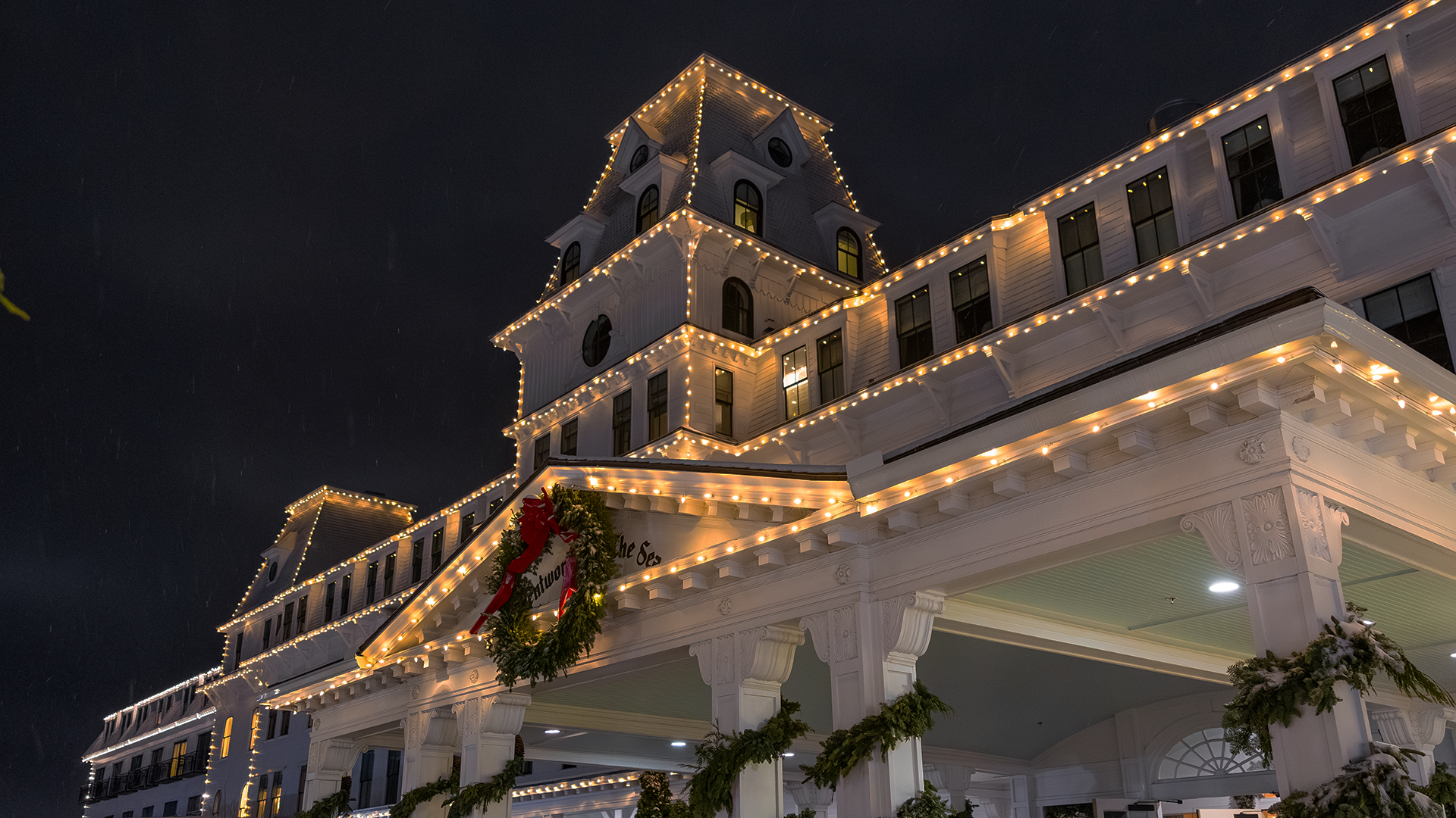 The Wentworth by the Sea hotel exterior at night, decorated with string lights and a large Christmas wreath.