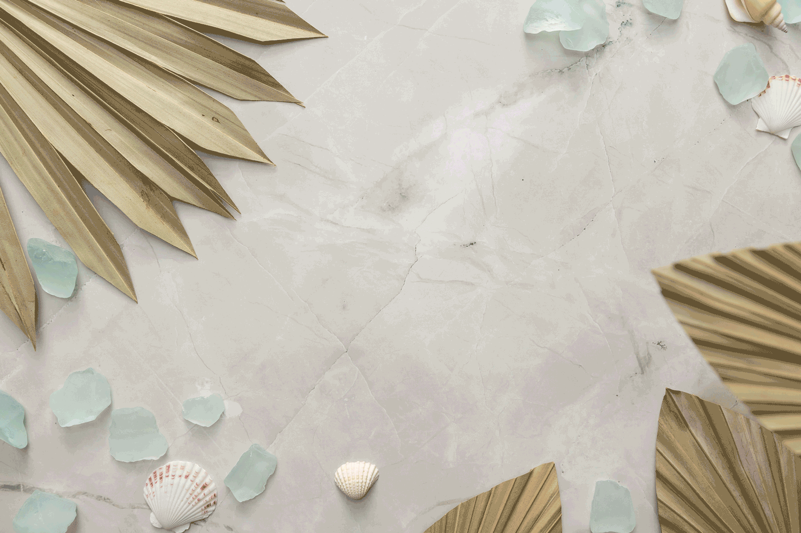 Dried palm leaves, light blue sea glass pieces, and white seashells arranged on a light marble surface with ample empty space in the center.