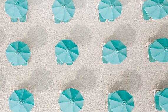 Aerial view of rows of turquoise beach umbrellas and white lounge chairs arranged neatly on a sandy beach.