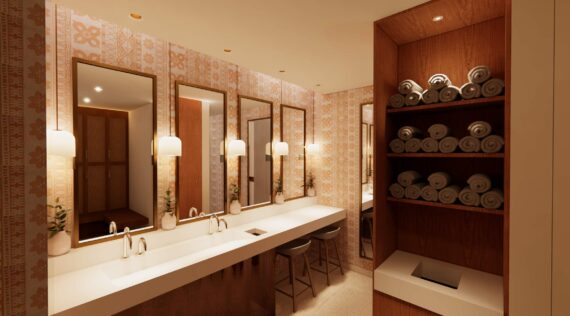 Modern bathroom with patterned wallpaper, three mirrors above a long white counter with sinks, stools, wall sconces, small plants, and shelves stacked with rolled towels. Warm, inviting lighting throughout the space.
