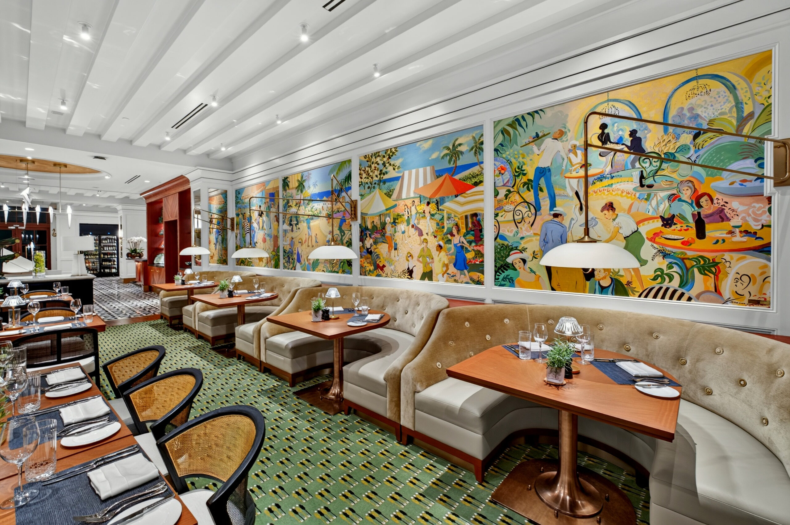 A stylish restaurant interior with tufted beige booths, wooden tables set for dining, and a vibrant mural depicting lively outdoor scenes along one wall. The atmosphere is elegant and colorful.