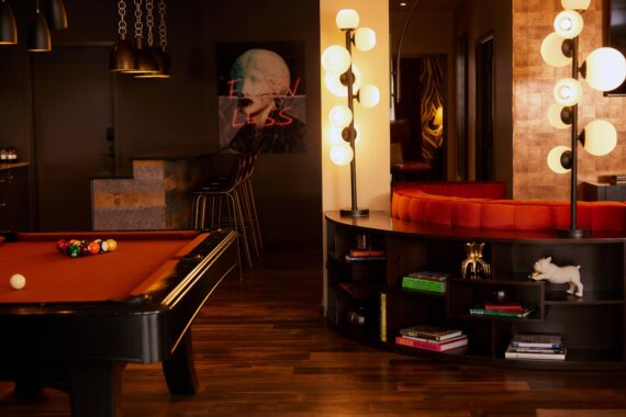 Two-bedroom suite living area at Bobby Nashville, featuring pool table, large velvet couch, novel lighting, and kitchen island with barstool chairs.