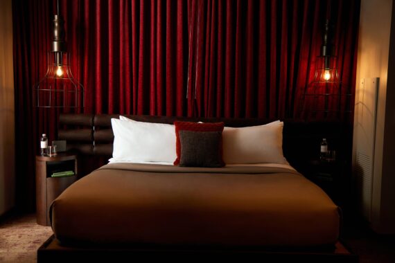 One of the king bedrooms in the two-bedroom suite at Bobby Nashville, showcasing the king bed, low lighting, and red velvet curtain backdrop.