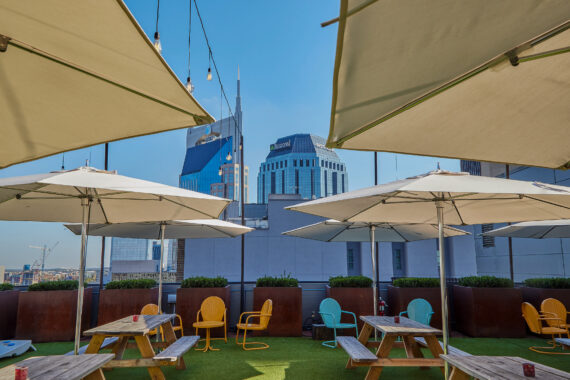 Picnic tables, umbrellas, and colorful seating overlooking the city at Rooftop Lounge.