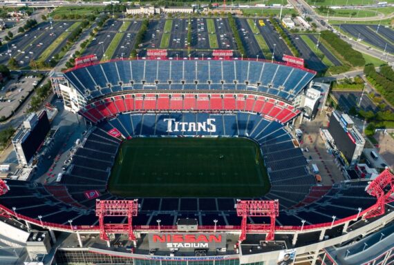Aerial view of Nissan Stadium, home of the Tennessee Titans, with blue and red seats, an empty football field, and surrounding parking lots in daylight.