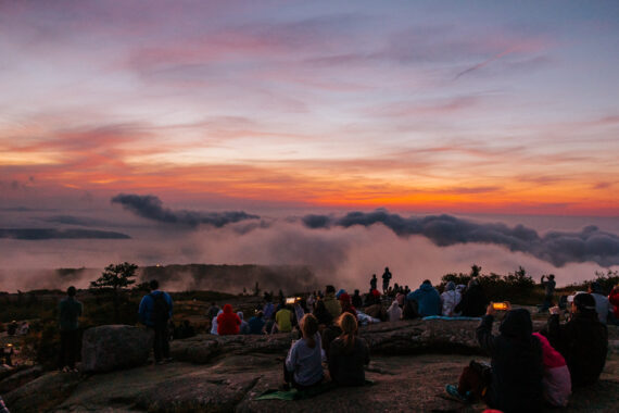 A group of nature enthusiasts gather at the summit of Cadillac Mountain at sunrise.