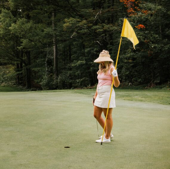 A women holds a golf flag by a hole.