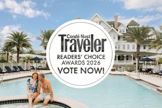 A couple sits on the edge of a resort pool, surrounded by palm trees and lounge chairs. Behind them is a large white house. Overlaid text reads: Condé Nast Traveler Readers Choice Awards 2026 Vote Now!.