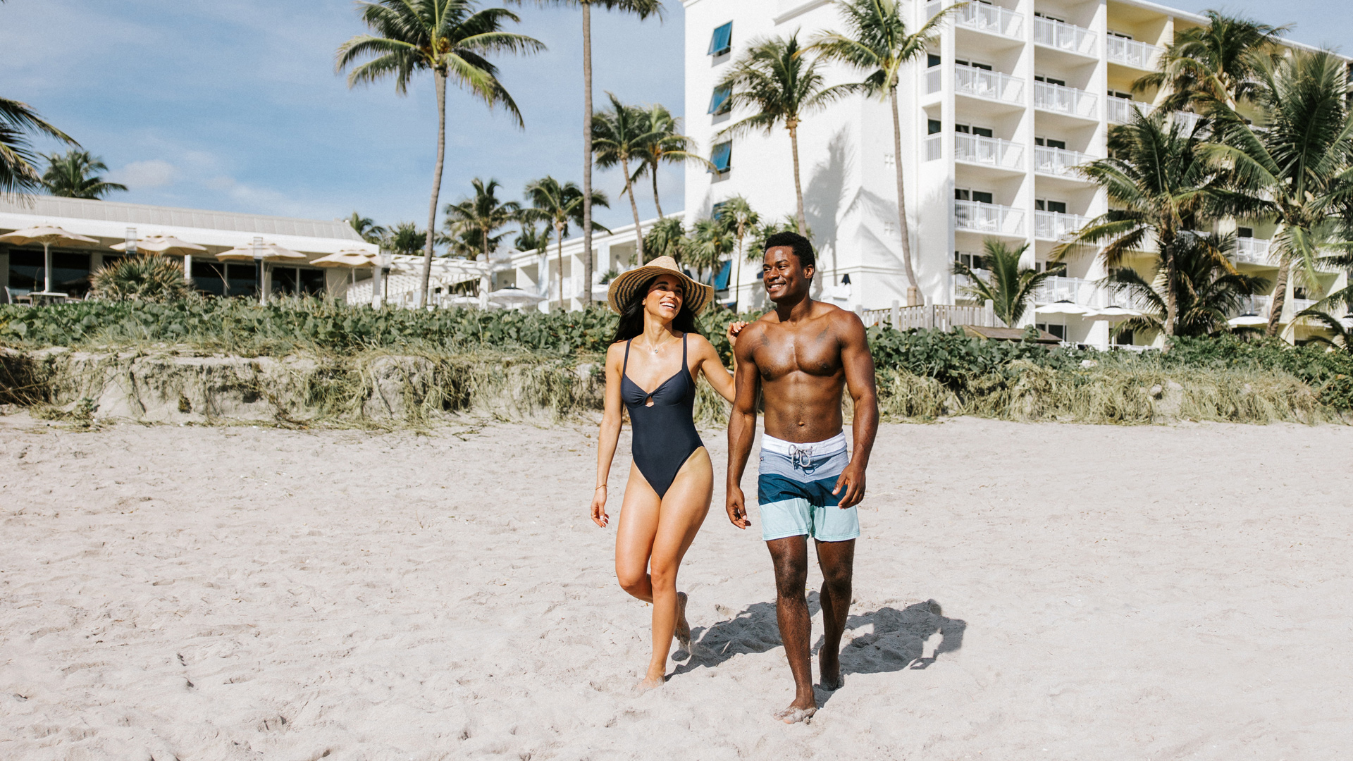 Happy couple walking on the beach with Delray Sands behind them