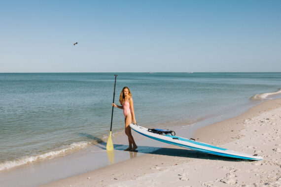 woman carrying a paddle board out to the ocean