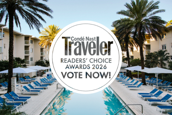 A resort pool lined with blue lounge chairs and white umbrellas, surrounded by palm trees and buildings. Overlaid is a Condé Nast Traveler Readers Choice Awards 2026 logo with the text Vote Now!.